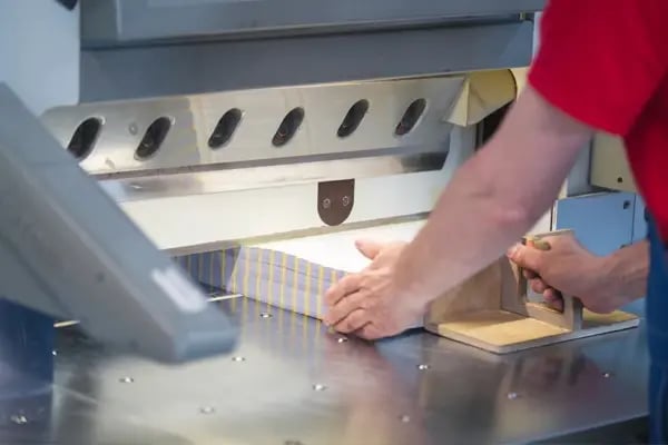 Hands of worker working on cutter guillotine machine in a printing factory